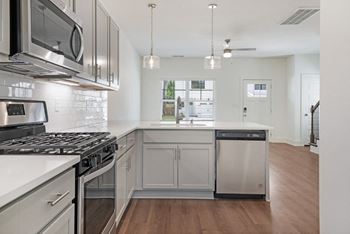 Modern kitchen with quartz countertops, backsplash, stainless appliances, and designer plank flooring.